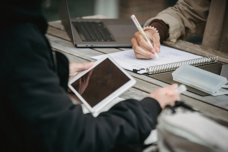 a couple of people sitting at a table with laptops, by Carey Morris, trending on pexels, lined paper, holding pencil, thumbnail, a wooden