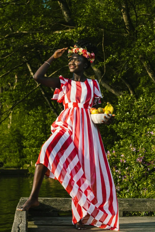 a woman standing on a dock holding a basket of fruit, an album cover, by Lily Delissa Joseph, shutterstock contest winner, red and white stripes, lady with glowing flowers dress, adut akech, at a fashion shoot