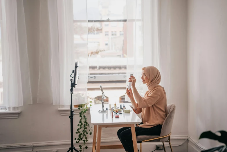 an old woman sits in a chair at a table with a camera in front of her