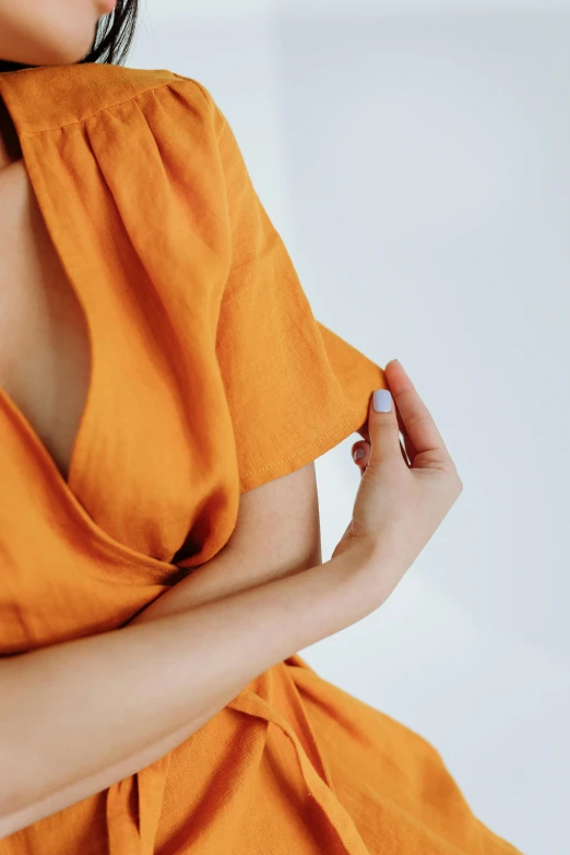 a woman in an orange dress posing for a picture, inspired by Christo, trending on pexels, linen, closeup of arms, detailed product image, curated collections