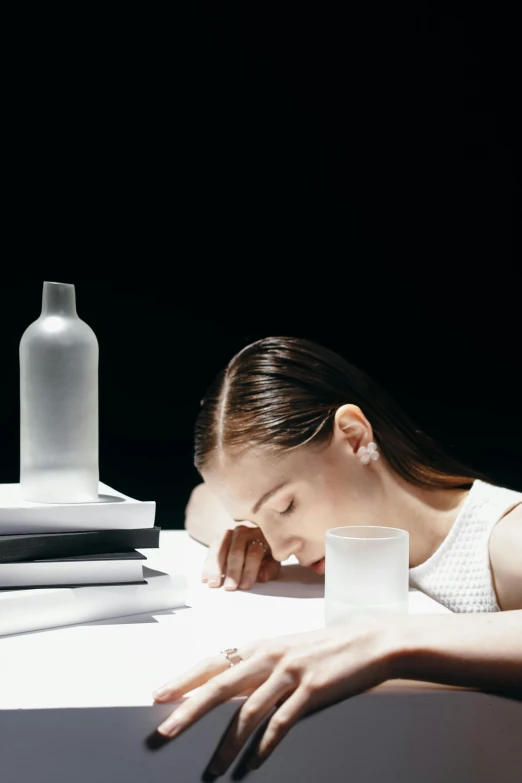 a woman sitting at a table with a glass of water, by Tadashi Nakayama, trending on unsplash, hyperrealism, asleep, water bottles, trying to study, in front of a black background