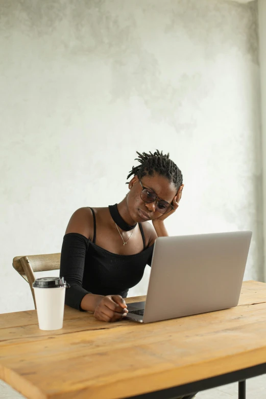 a woman sitting at a table with a laptop, by Carey Morris, trending on pexels, afrofuturism, wearing a cropped tops, post graduate, sad look, shades