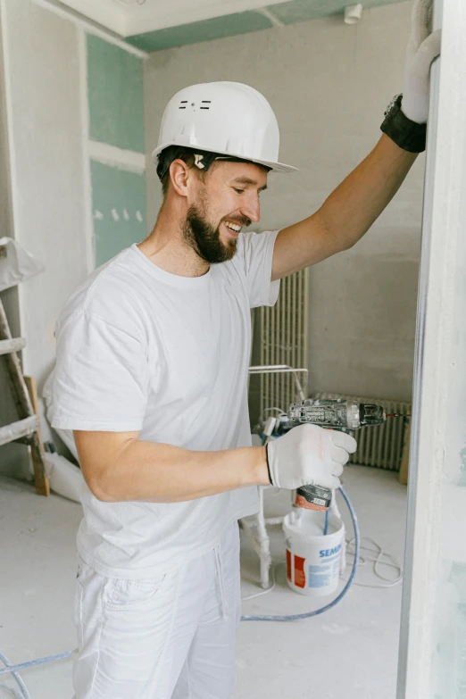 a man is painting a wall in a room, hard hat, lean man with light tan skin, man in white t - shirt, wearing plumber uniform