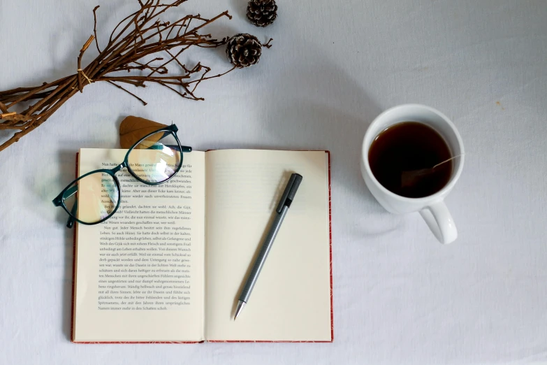 a book, reading glasses and coffee sit on top of a table