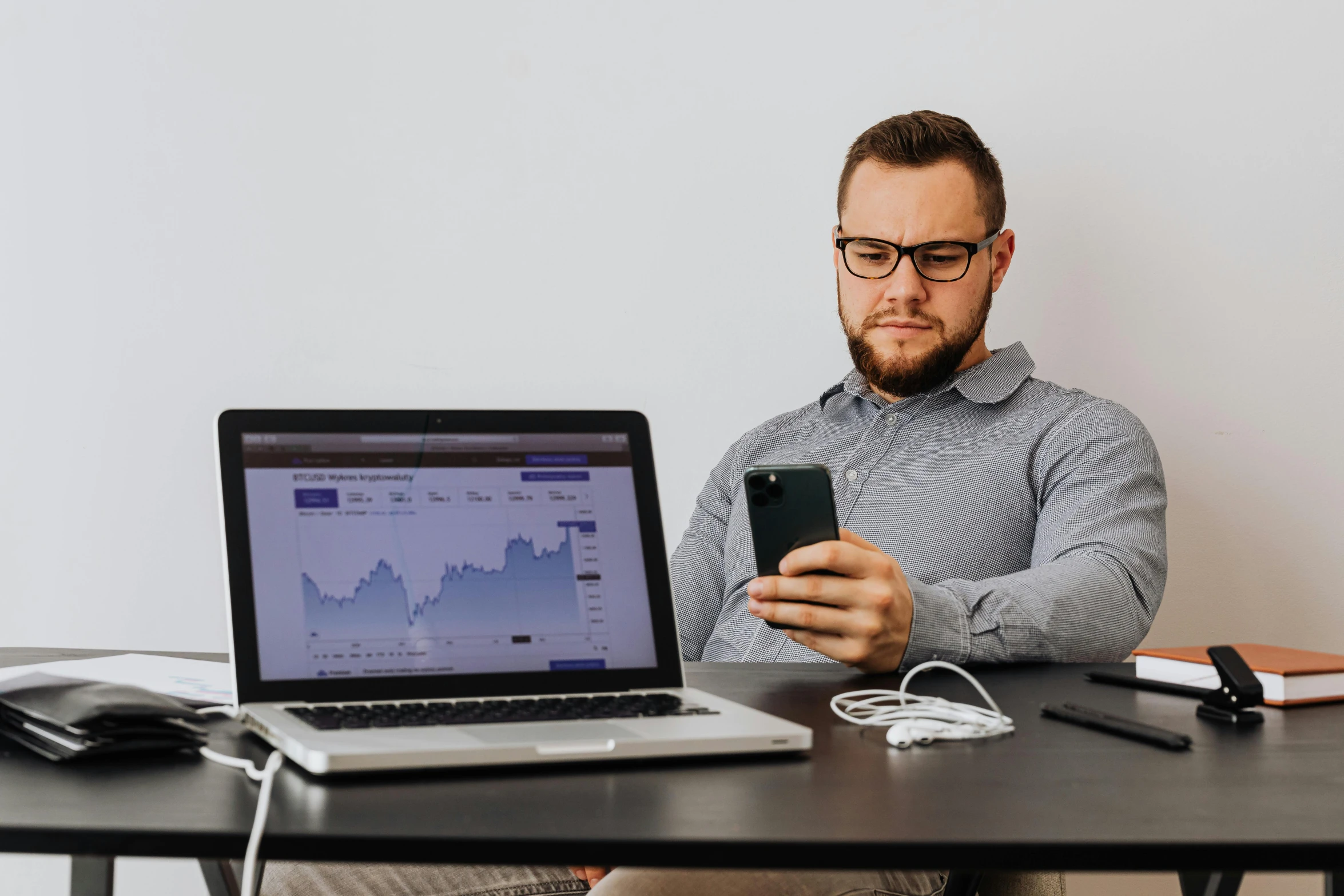 a man sitting at a table with a laptop and cell phone, by Adam Marczyński, trending on pexels, analytical art, typical cryptocurrency nerd, with nerdy glasses and goatee, trading stocks, thumbnail