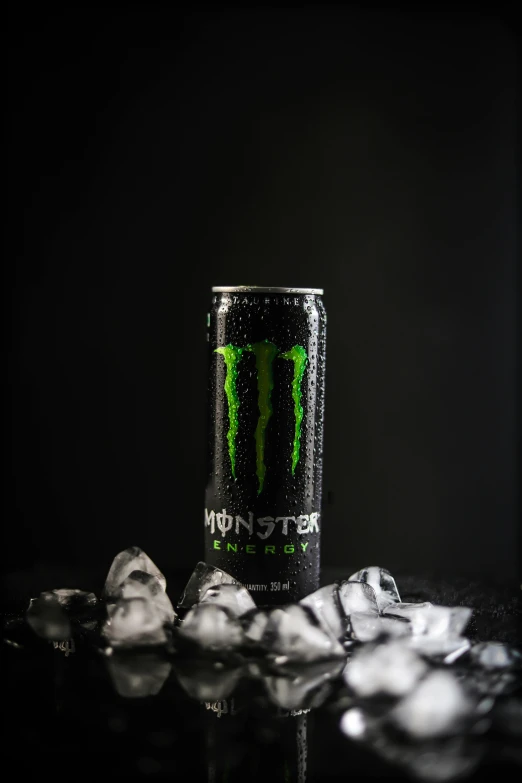 a monster energy drink sitting in a can with ice cubes next to it