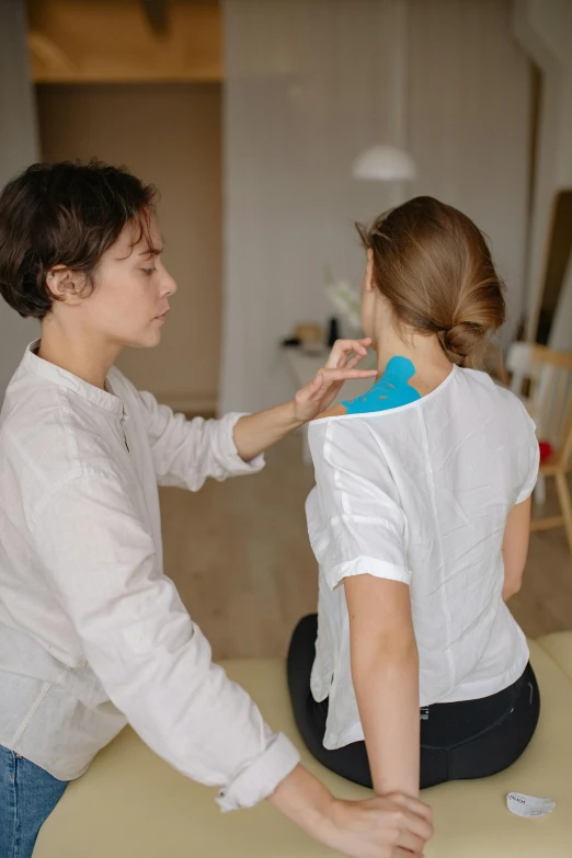 a woman sitting on top of a table next to a woman, silicone skin, shoulder pads, medical image, human design