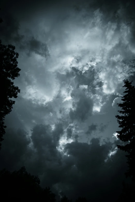 a black and white photo of a cloudy sky, unsplash, romanticism, dark forests surrounding, colorfully ominous background, dark blue sky, taken in the late 2000s