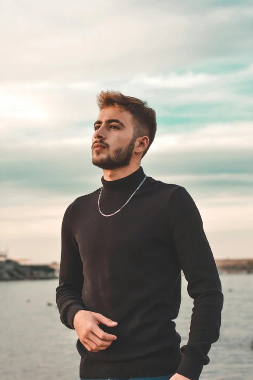 young man with necklace standing in front of the ocean