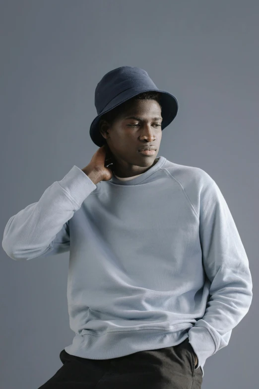 a man sitting on a stool wearing a hat, blue sweater, grey backdrop, obunga, wearing a track suit