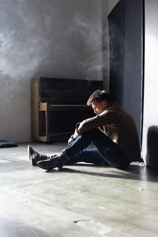 a man sitting on the floor smoking a cigarette, trending on pexels, visual art, portrait of depressed teen, light over boy, trapped in the backrooms, hugging his knees