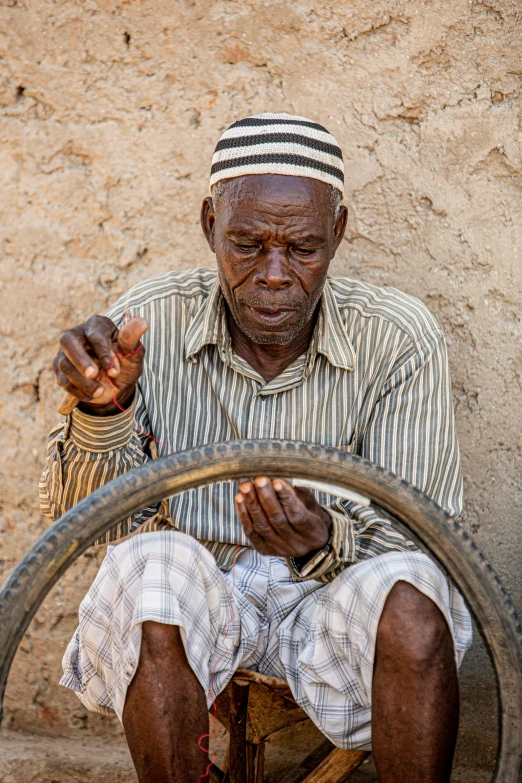 a man sitting on the ground with a bicycle wheel, intricate african jewellery, old man doing hard work, 2019 trending photo, ultra texture