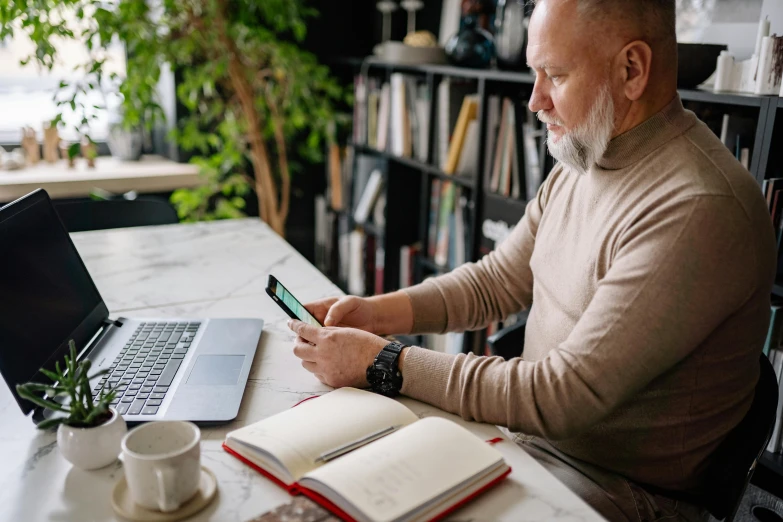 a man sitting at a table with a laptop and cell phone, pexels contest winner, short white beard, book library studying, middle aged balding superhero, avatar image