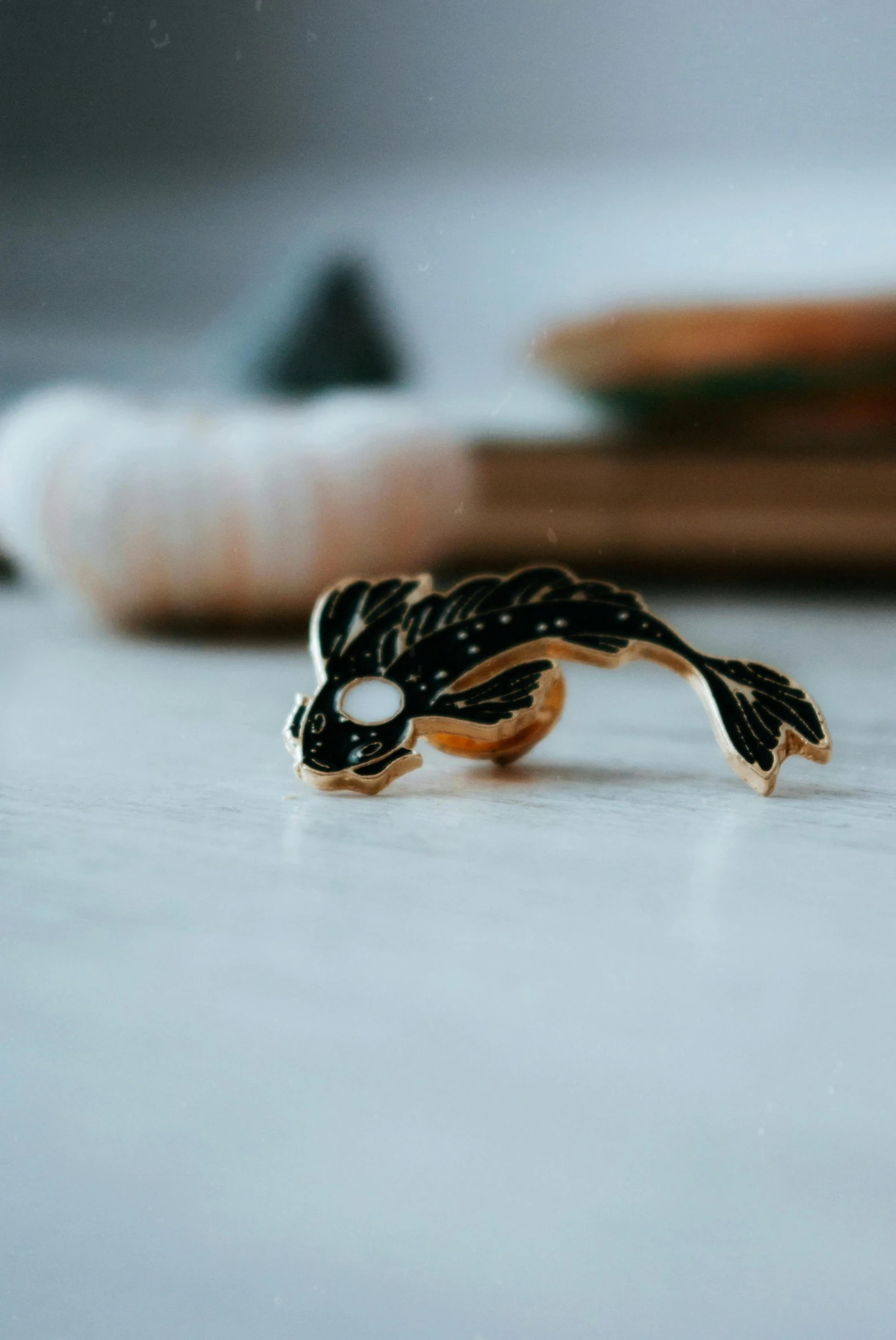 a close up of a figurine of a fish on a table, a macro photograph, inspired by Kanō Hōgai, unsplash, pins, ring, carbon black and antique gold, detailed silhouette