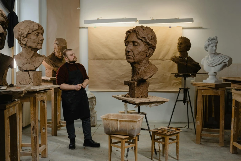 a man standing in front of a bunch of busts, pexels contest winner, academic art, tredning on art station, hard clay, portrait of a female art student, ivan laliashvili