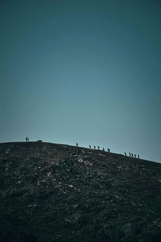 a group of people standing on top of a hill, by Alexis Grimou, unsplash contest winner, minimalism, blue and black, miners, wolf pack following, seen from a distance