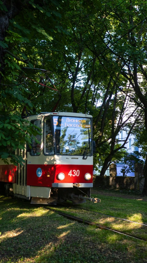 a red and white train traveling through a lush green forest, inspired by Otakar Sedloň, street tram, exterior, cccp, square