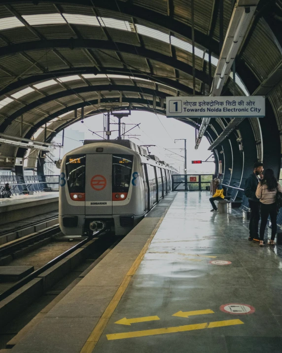 a train pulling into a train station next to people, beautiful futuristic new delhi, 🚿🗝📝, lgbtq, in a subway