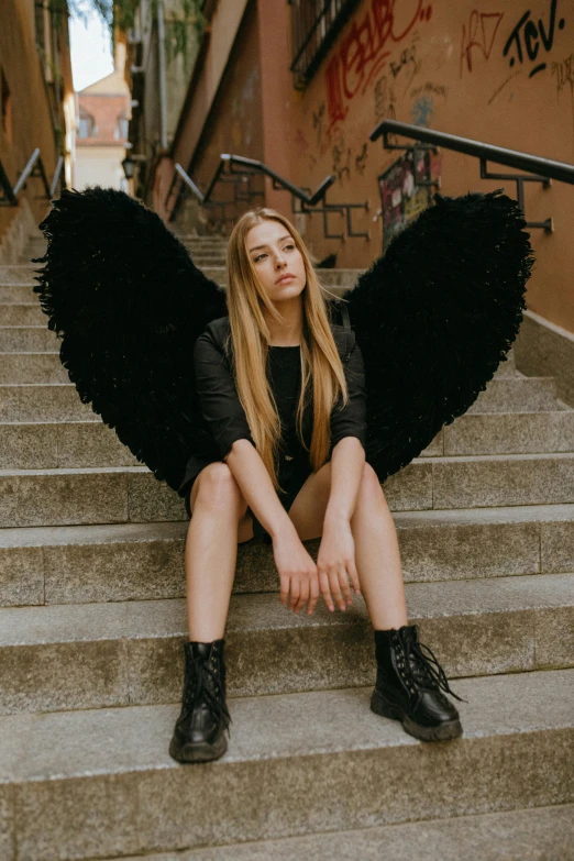 a woman with black wings sitting on a flight of stairs, by Marie Angel, pexels contest winner, portrait of kim petras, girl with angel wings, young teen, cupid