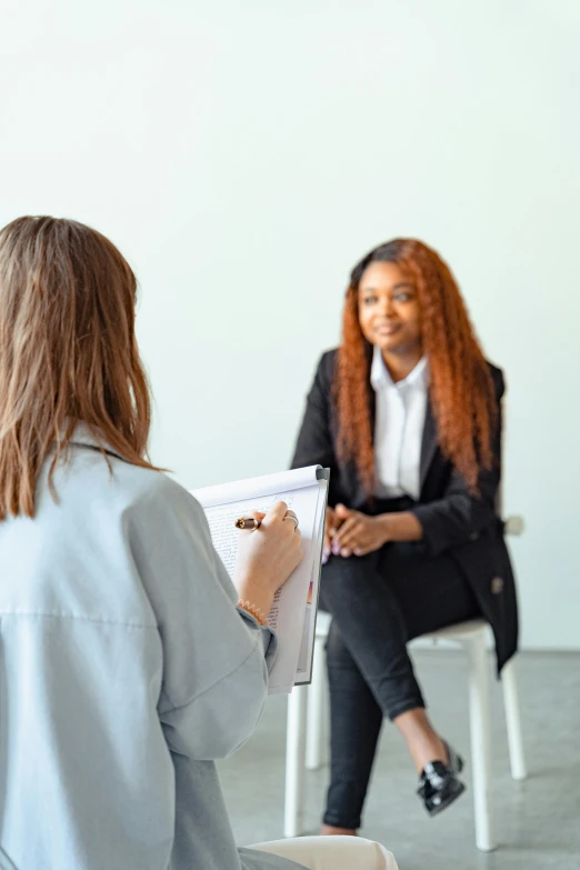 two women sitting in chairs talking to each other, holding a clipboard, clinically depressed, varying ethnicities, girl in suit