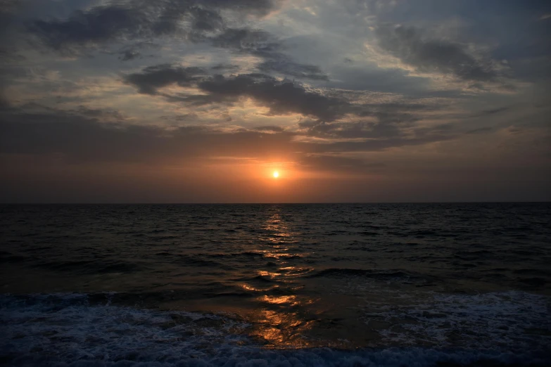 the sun setting on the water with some clouds