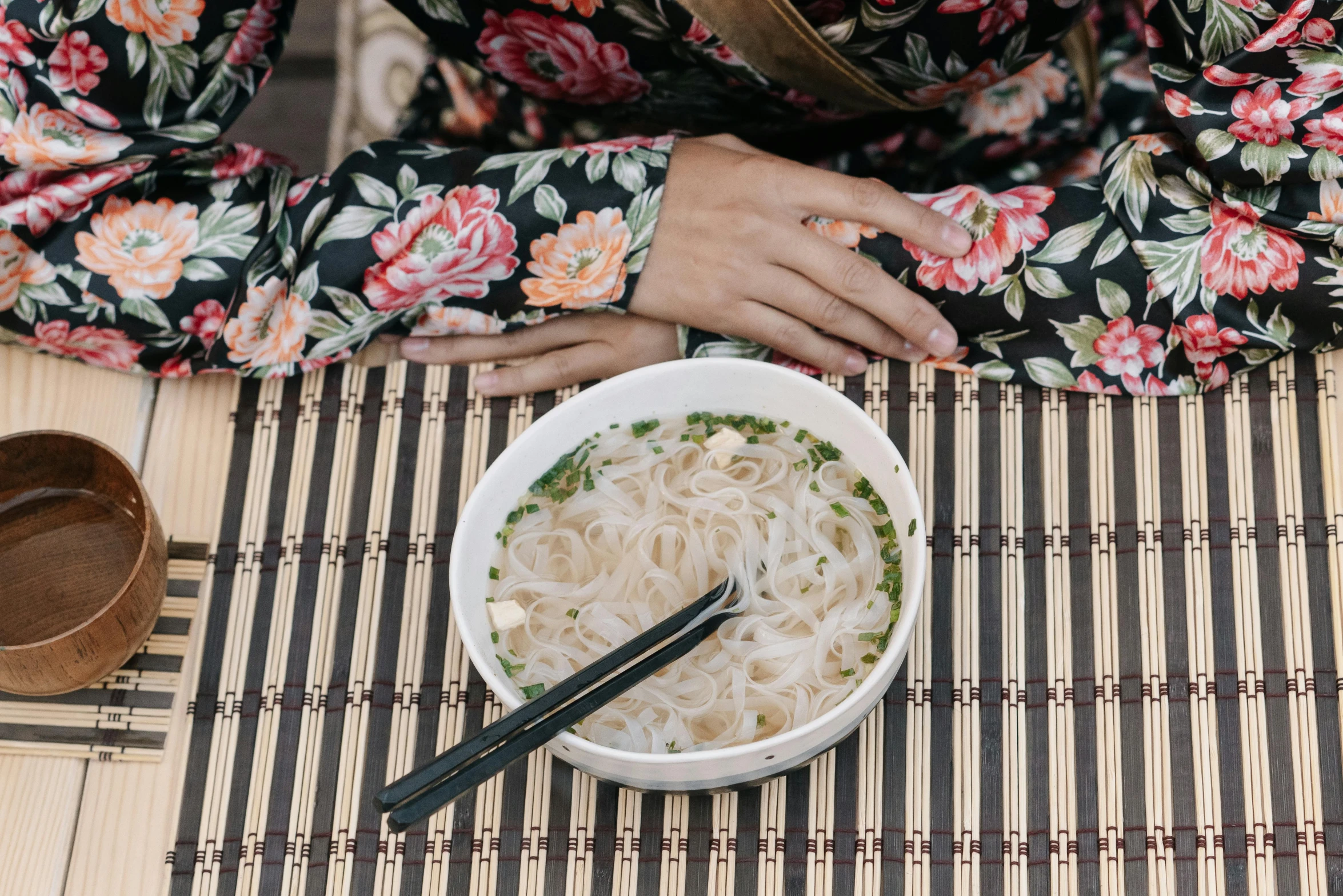 a person eating noodles in a bowl on top of a mat