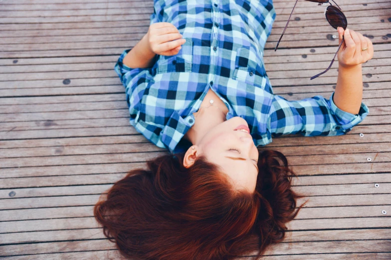 a woman laying on top of a wooden floor, trending on unsplash, wearing plaid shirt, ( redhead, blue, realistic »