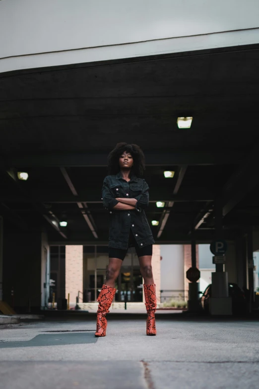 a woman in a black dress and red boots, by Lily Delissa Joseph, pexels contest winner, afrofuturism, in front of a garage, sza, looking straight, lightening