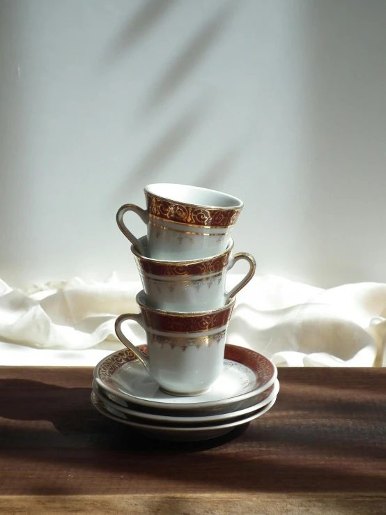 a stack of coffee cups sitting on top of a wooden table, gold and red filigree, vintage inspired, set in 1992 japan, jovana rikalo