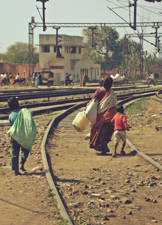 a group of people walking along a train track, by Rajesh Soni, poverty, instagram picture, bright sunny day, maternal