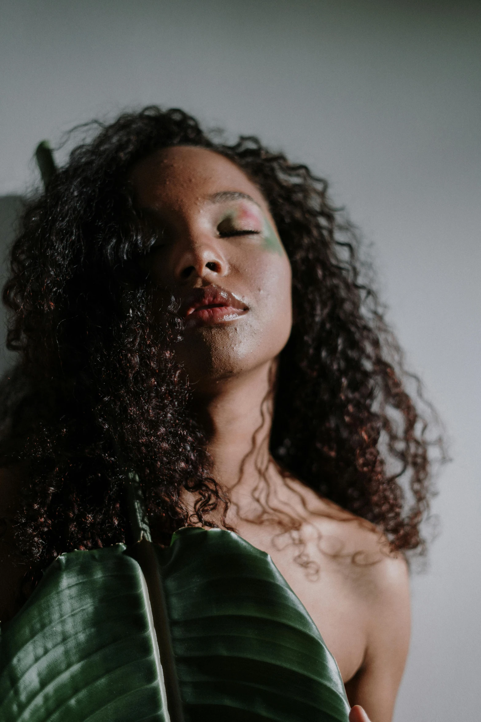 a woman holding a large green leaf in front of her face, an album cover, trending on pexels, renaissance, a black man with long curly hair, pearlescent skin, ( low key light ), body portrait