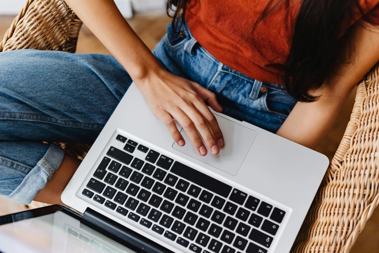 a woman sitting on a wicker chair using a laptop, trending on pexels, sitting on a red button, holding an epée, student, sitting with wrists together