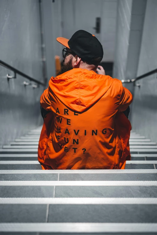 a man in an orange jacket sitting on a set of stairs, inspired by Mike Winkelmann, trending on pexels, happening, streetwear, back turned, with prison clothing, awestriking