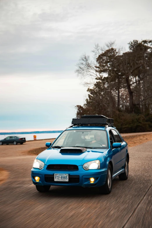 a blue car driving down a road next to a beach, a picture, with a roof rack, slight overcast lighting, avatar image, subaru