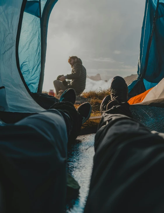 a couple of people sitting inside of a tent, trending on unsplash, legs taking your pov, in the rain, best photo, sleeping bag