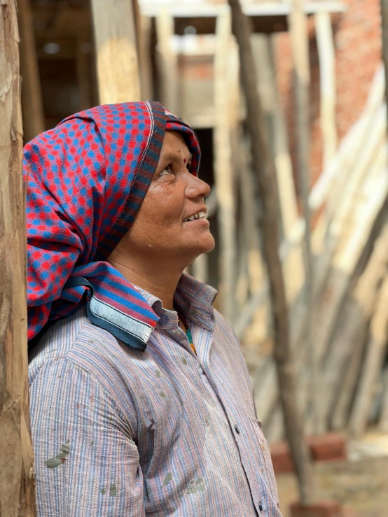 a woman standing next to a wooden pole, peaked wooden roofs, woman's face looking off camera, very vibrant, construction