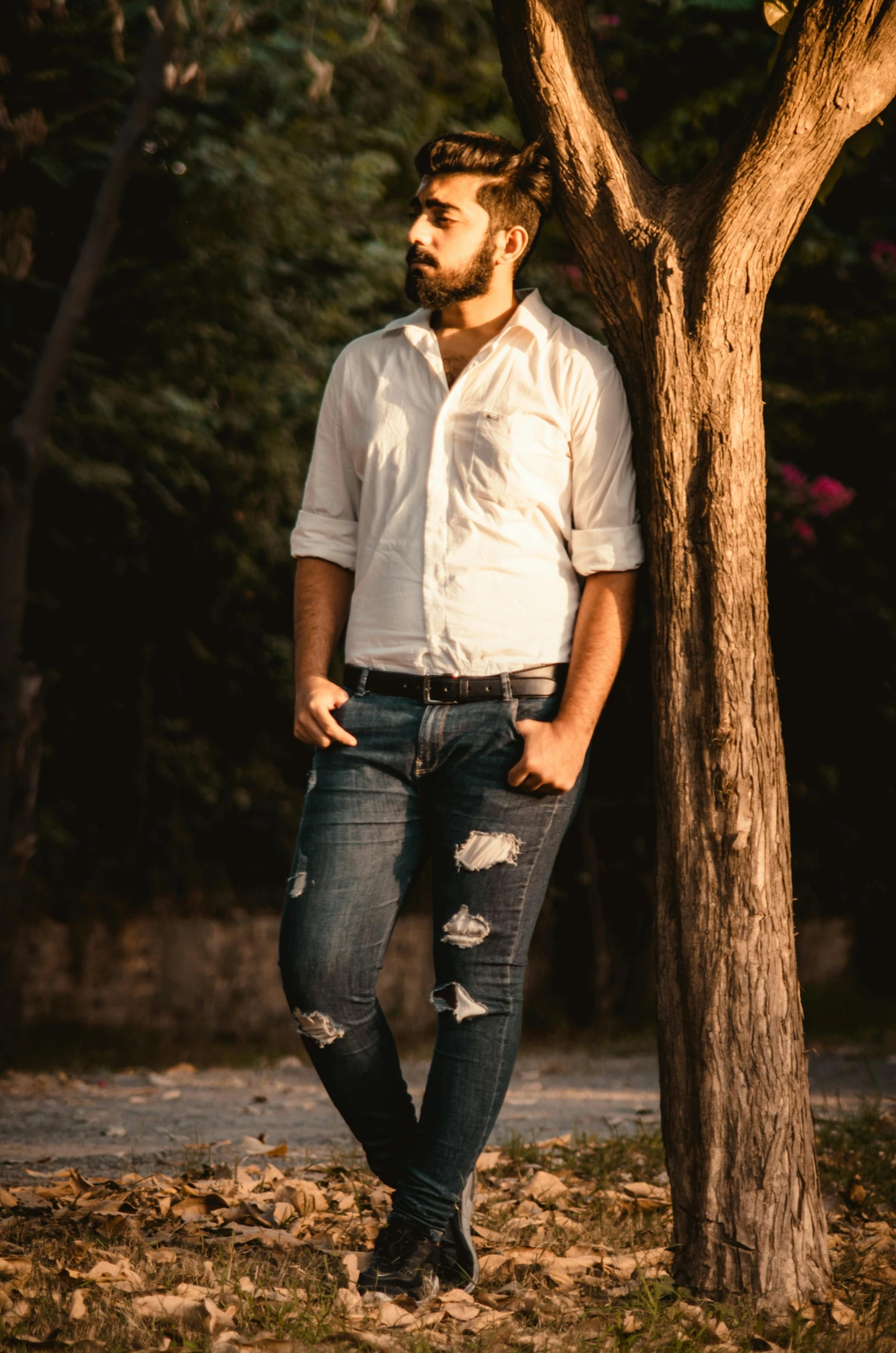 a man in a white shirt leaning against a tree