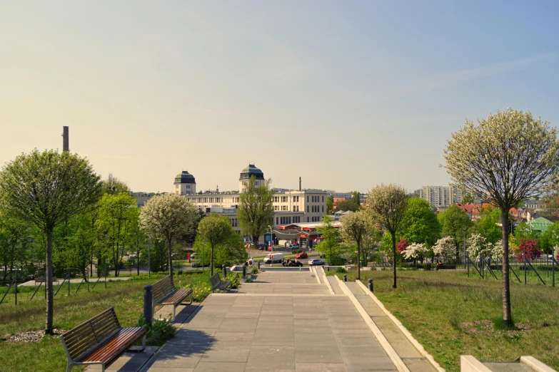 a park with benches and a building in the background, by Julia Pishtar, pexels contest winner, art nouveau, rostov city, panoramic shot, green square, walking to the right