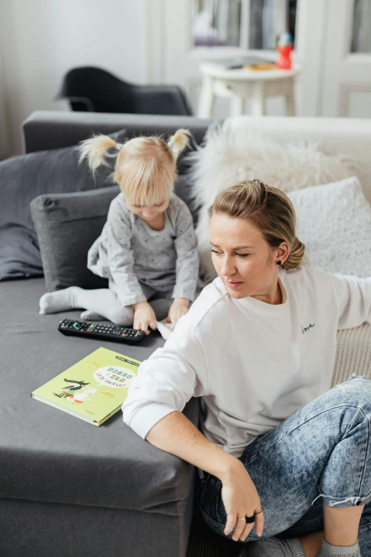 a woman sitting on top of a couch next to a child, holding notebook, zellk, swedish, monthly