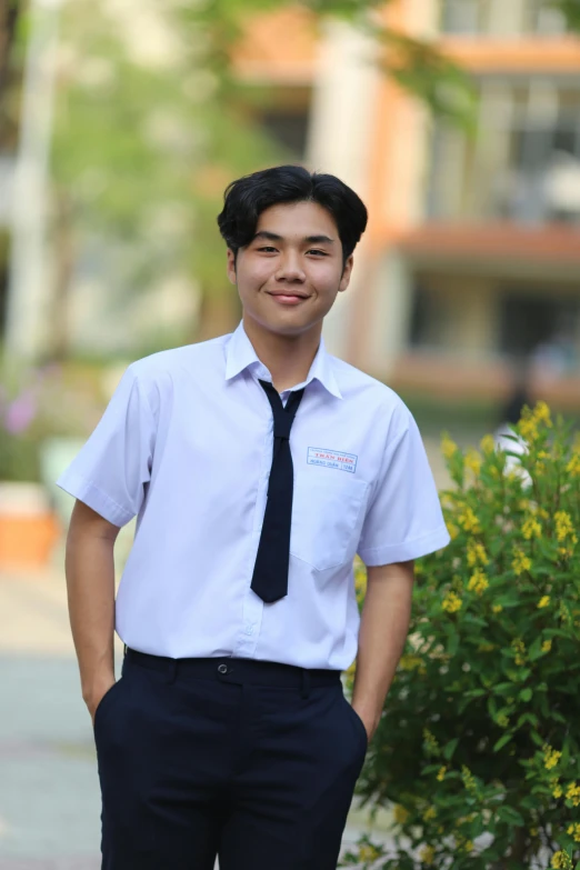 a smiling schoolboy in formal attire stands outside