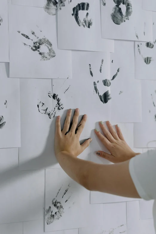 a woman standing in front of a wall covered in hand prints, an ink drawing, trending on pexels, hands on counter, on white paper, playing, set pieces