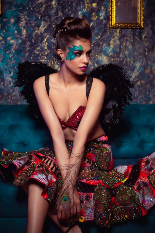 a woman sitting on top of a blue couch, inspired by Gabriel Ba, trending on pexels, renaissance, red feathered wings, indian super model, multicoloured, wings black lace wear