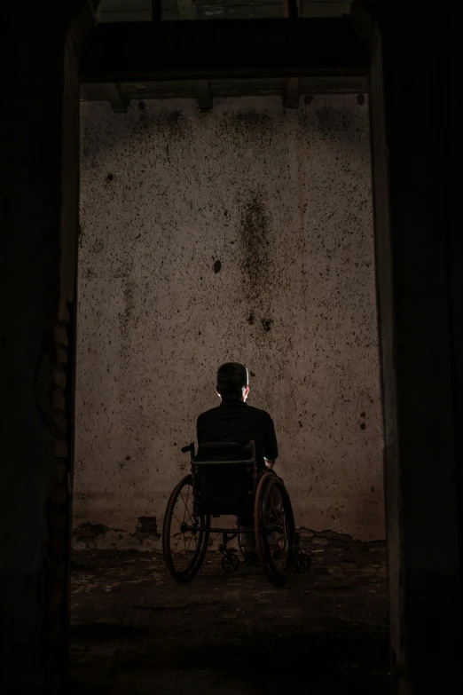 a man in a wheelchair in a dark room, an album cover, pexels contest winner, conceptual art, eerie back light, ( ( theatrical ) ), dark building, 8 k movie still