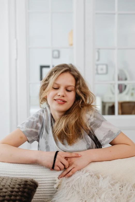 a woman sitting on a bed with her eyes closed, by Louisa Puller, trending on unsplash, portrait of normal teenage girl, on a white table, smiling confidently, high-quality photo