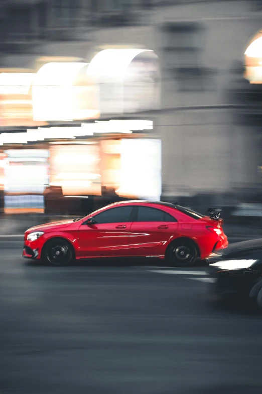 a red car driving past a car in a busy street