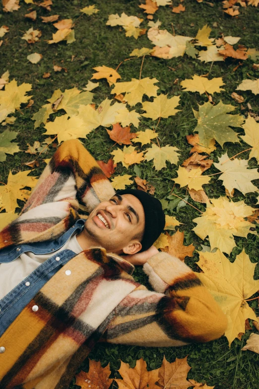 a man laying on top of a pile of leaves, an album cover, trending on pexels, satisfied pose, yellow clothes, happy cozy feelings, high quality screenshot