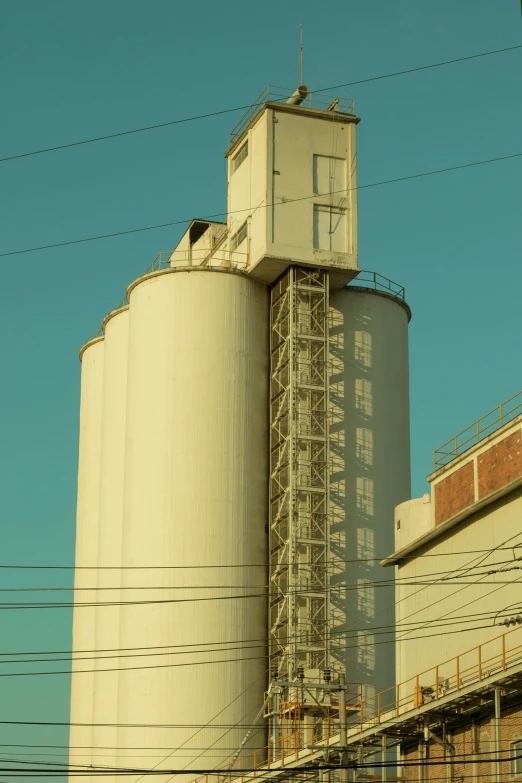 a large white grain silo sitting next to a building, a photo, flickr, photorealism, late afternoon sun, machinery and wires, minimalistic aesthetics, elevator