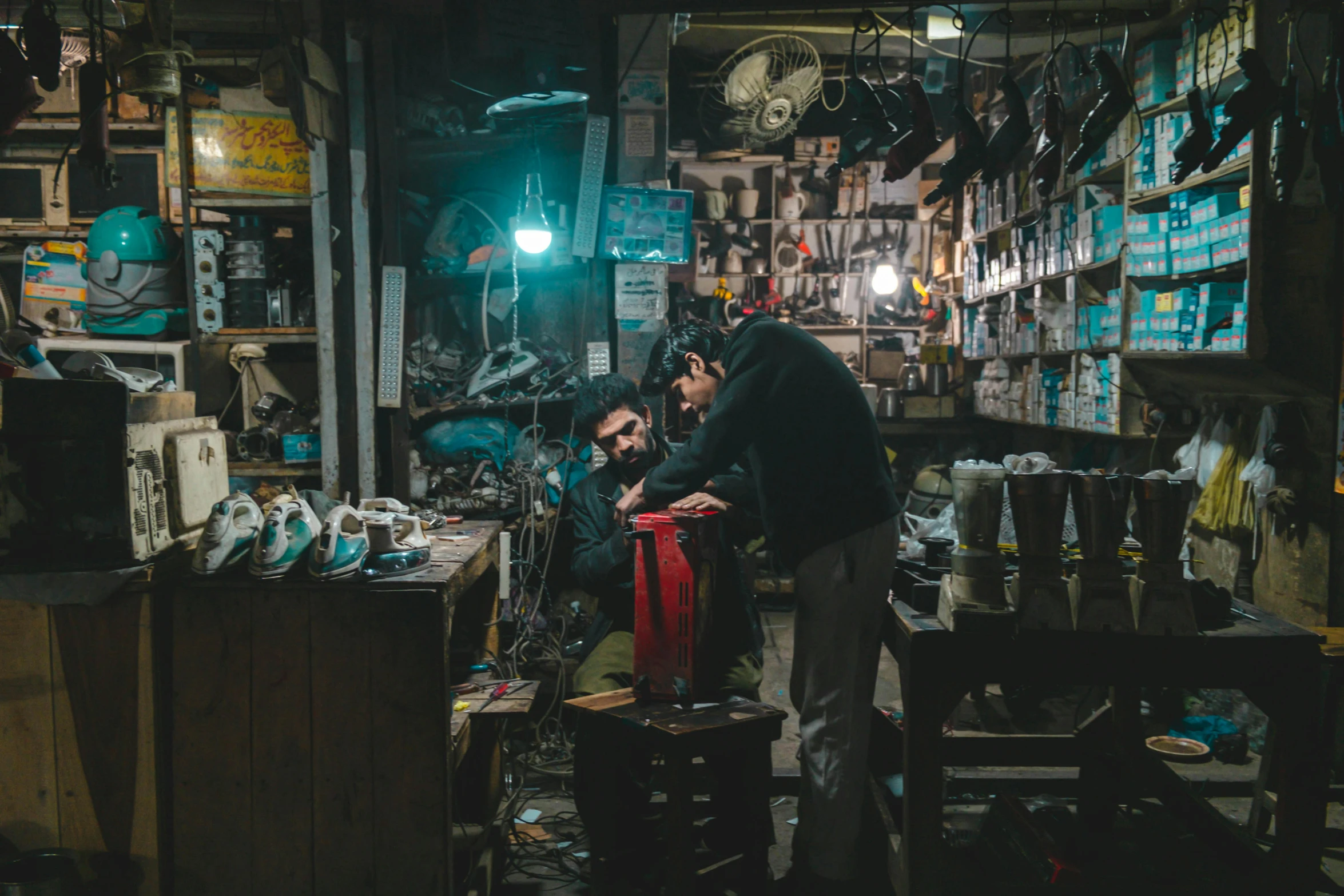 a couple of men standing next to each other in a room, pexels contest winner, shin hanga, sitting on a store shelf, spare parts, busy night, working in the forge