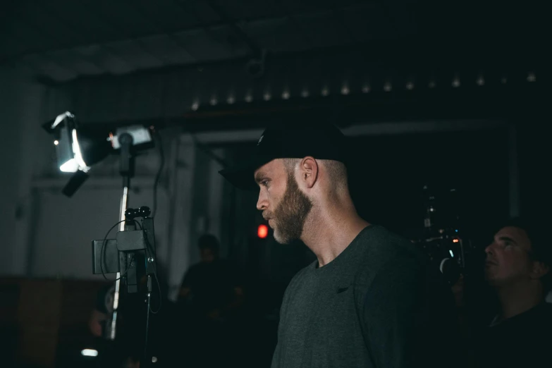 a man standing in front of a microphone, a picture, by Robbie Trevino, vsco, low quality footage, light beard, behind the scenes photo