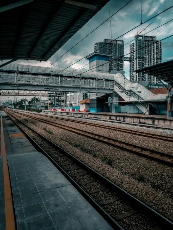 a train station with train tracks and buildings in the background, inspired by Thomas Struth, unsplash contest winner, malaysian, low quality photo, cinematic. by leng jun, overcast day